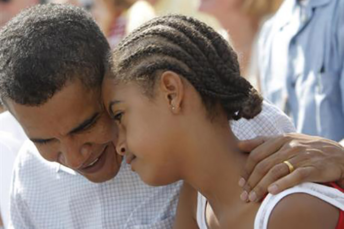 FILE - In this July 4, 2008 file photo, then-Democratic presidential candidate, Sen. Barack Obama, D-Ill. talks to his daughter Malia as they watch an Independence Day parade in Butte, Mont. President Barack Obama’s daughter Malia was just 10 and longing for a promised puppy when her family moved into the White House. She’s marked some of life’s milestones in the past seven years, and another one comes Friday: graduation from high school. (AP Photo/Jae C. Hong, File)