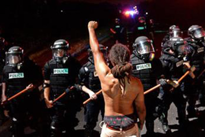 A protester stands with his left arm extended and fist clenched in front of a line of police officers in Charlotte, N.C. on Tuesday, Sept. 20, 2016. Authorities used tear gas to disperse protesters in an overnight demonstration that broke out Tuesday after Keith Lamont Scott was fatally shot by an officer at an apartment complex. (Jeff Siner/The Charlotte Observer via AP)