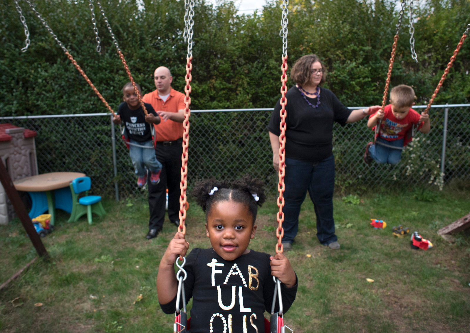 Josh and Meg McKivigan give their adopted children (left to right) twins Ezra and Naomi, 3, and Eli, 4, a push on the swings behind their Bellevue home. (Photo by Martha Rial/PublicSource)