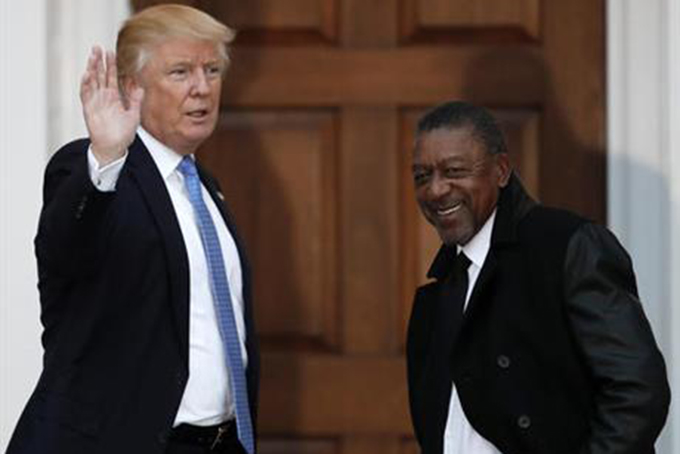 FILE - In this Nov. 20, 2016 file photo, President-elect Donald Trump stands with BET founder Robert Johnson at the Trump National Golf Club Bedminster clubhouse in Bedminster, N.J.. Johnson is one of dozens of people who have paraded into Trump’s properties in New York and New Jersey in recent weeks for job interviews and other consultations with the Republican. Several described the meetings as serious, yet conversational, with the president-elect leading the discussion and asking questions extemporaneously, without consulting notes. (AP Photo/Carolyn Kaster, File)