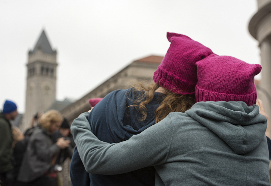Protestors wearing punk pussy hats embrace near the new Trump International Hotel during Women’s March on Washington in Washington D.C. (Photo by Martha Rial for PublicSource)