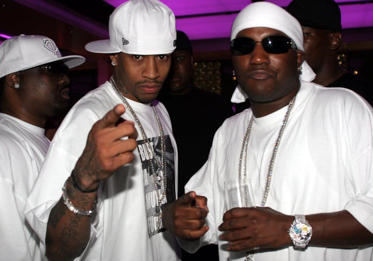 Three men wearing white hats, white T-shirts and diamond jewelry stand together