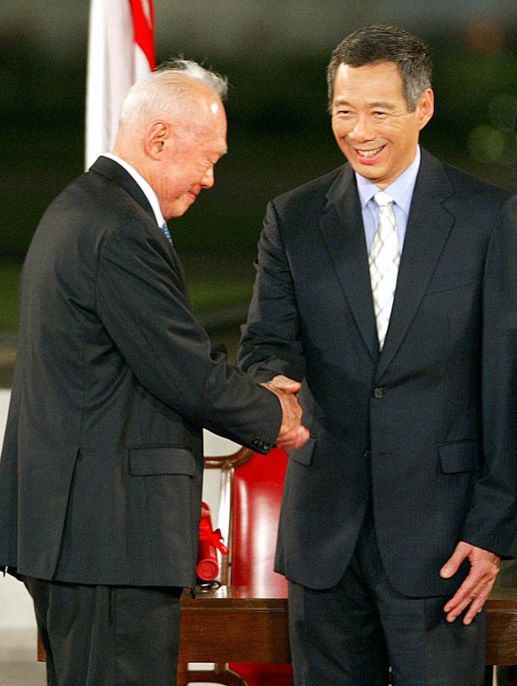 Two men in suits, one older, one younger, shaking hands.