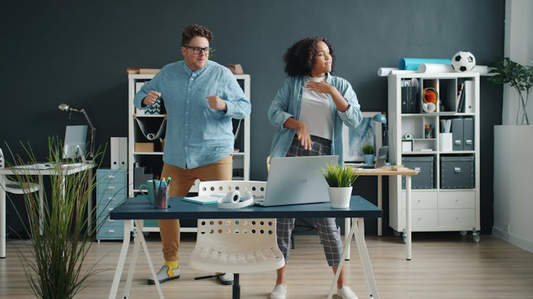 Two people standing behind a desk, doing light exercise
