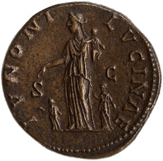 An old coin with a woman in the center with two children on either side and one on her shoulder.
