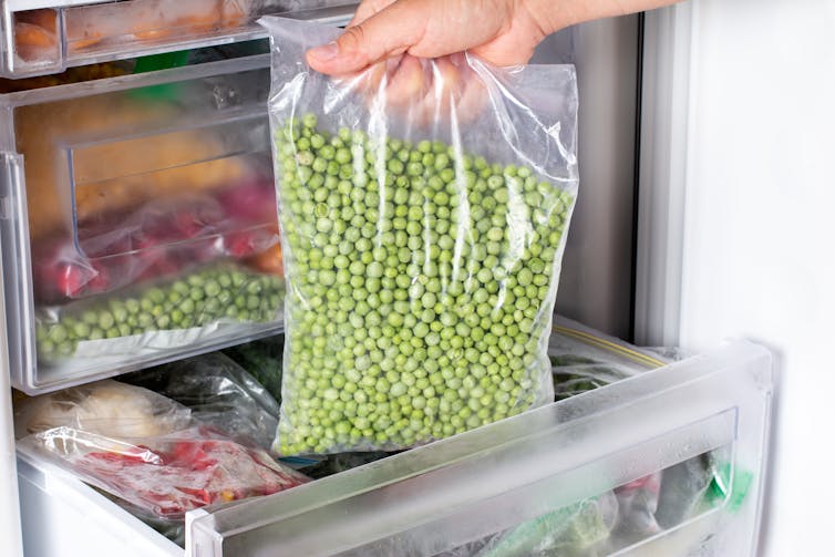 A person's hand pulls out a bag of peas from the freezer.