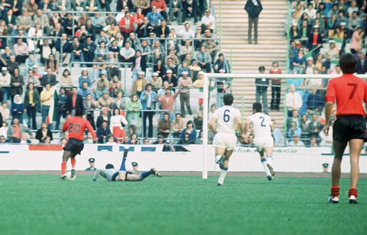 A group of men in white and orange jerseys stand on a football pitch.