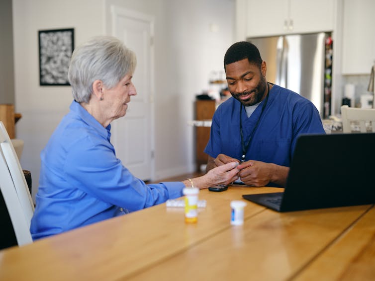 A home health provider attends to an older patient in her home.