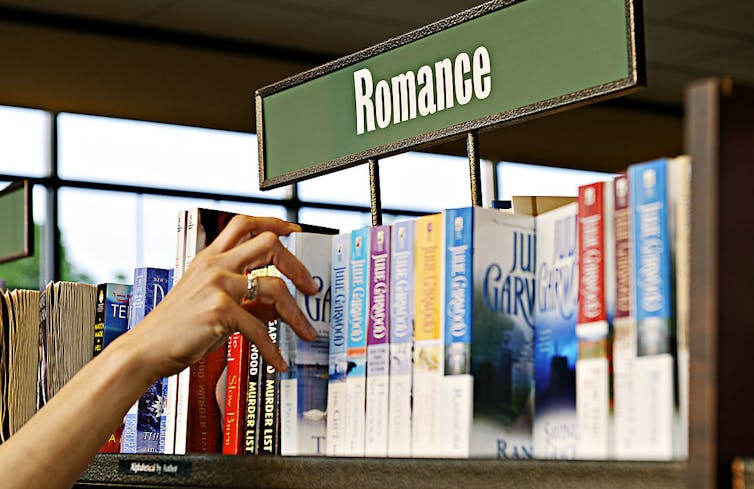 A hand reaching for a book on a shelf titled 'Romance.'