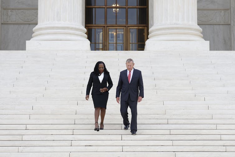 A Black woman and white man walk down steps in front of a federal building.