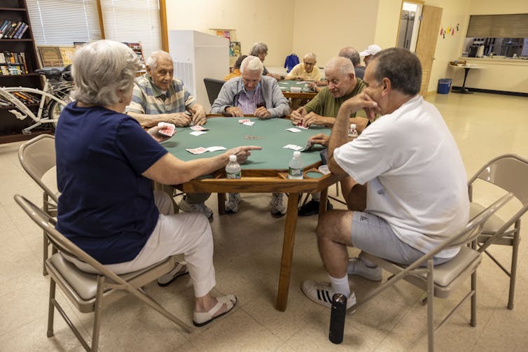 A group of people sit around a table and play cards.