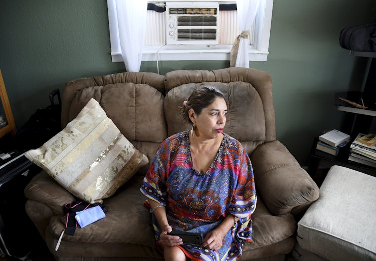 A woman sits on a couch underneath an air conditioner.